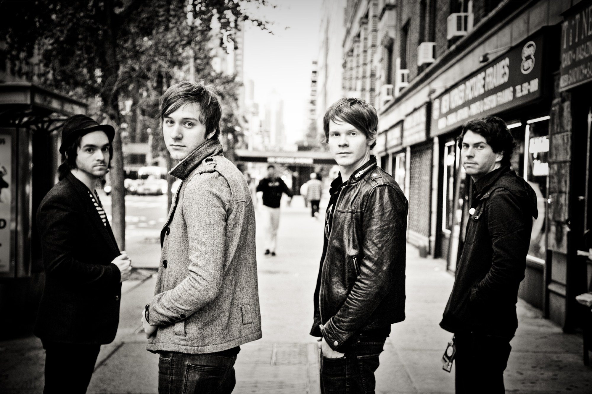 Black-and-white portrait of a four-piece band on a Manhattan sidewalk, each turning back toward the camera