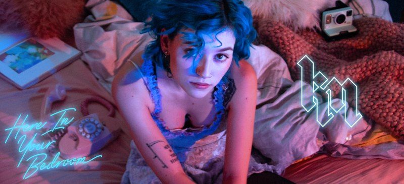 Social promo: the artist on a bed under blue light with neon script